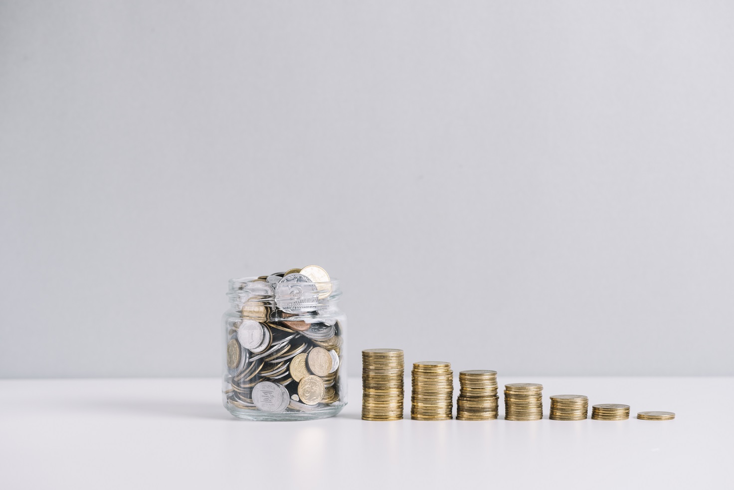 Ternyata Koin Bisa Jadi Investasi Jangka Panjang! 4 glass jar full money front decreasing stacked coins against white background