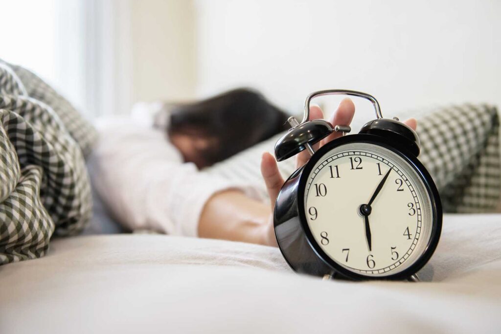 sleepy woman reaching holding alarm clock