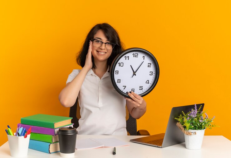 Maba Wajib tahu! Ini Dia 5 Tips Dalam Membagi Waktu Kuliah dan Berorganisasi 6 young smiling pretty caucasian schoolgirl wearing glasses sits desk with school tools puts hand face holds clock isolated orange space with copy space 141793 60021