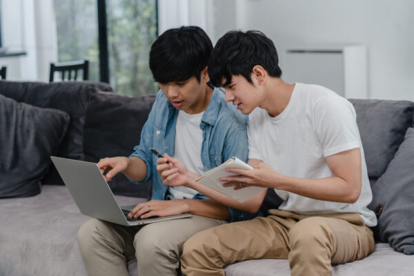 young asian gay couple working laptop modern home asia lgbtq men happy relax fun using computer analyzing their finances internet together while lying sofa living room house