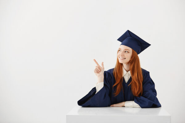 young female university graduate academic cap sitting table smiling pointing left future lawyer engineer showing idea