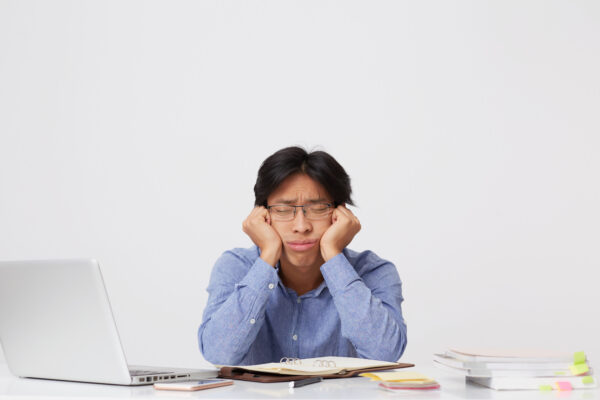 tired sleepy asian young business man glasses with head hands sitting sleeping workplace table white wall
