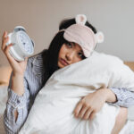 Kesulitan Untuk Tidur Nyenyak? Lakukan 2 Hal Ini Agar Kualitas Tidurmu Lebih Baik 5 sad girl pajamas sleep mask is hugging white pillow holding alarm clock
