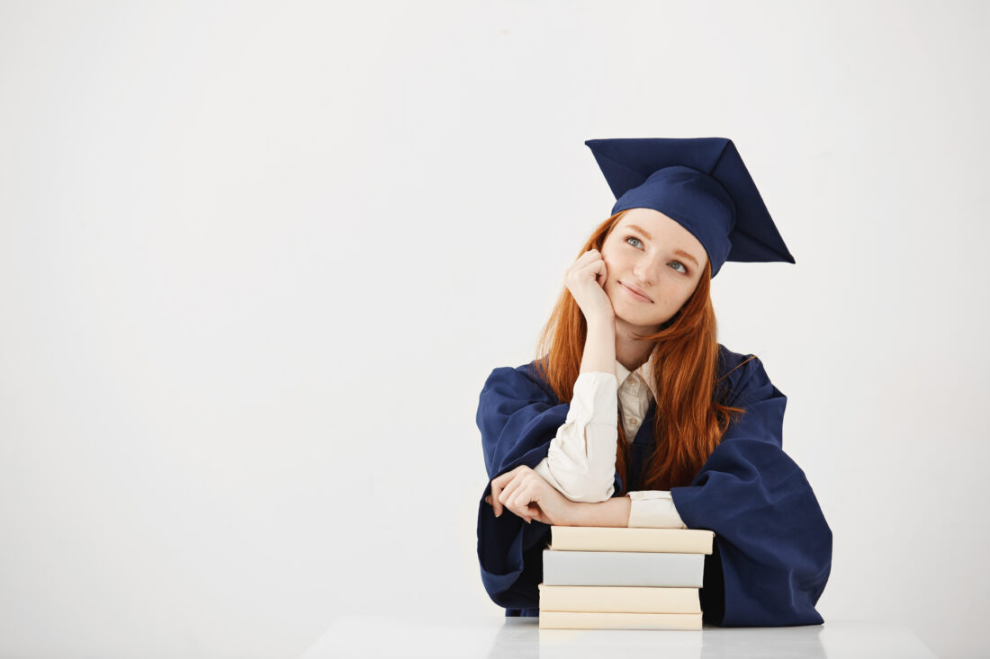 dreamy graduate woman smiling thinking sitting with books