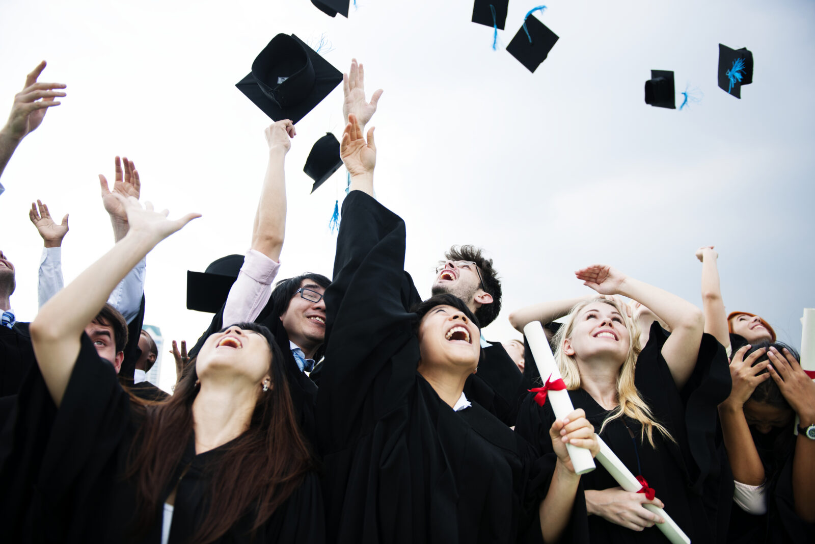 group diverse grads throwing caps up sky