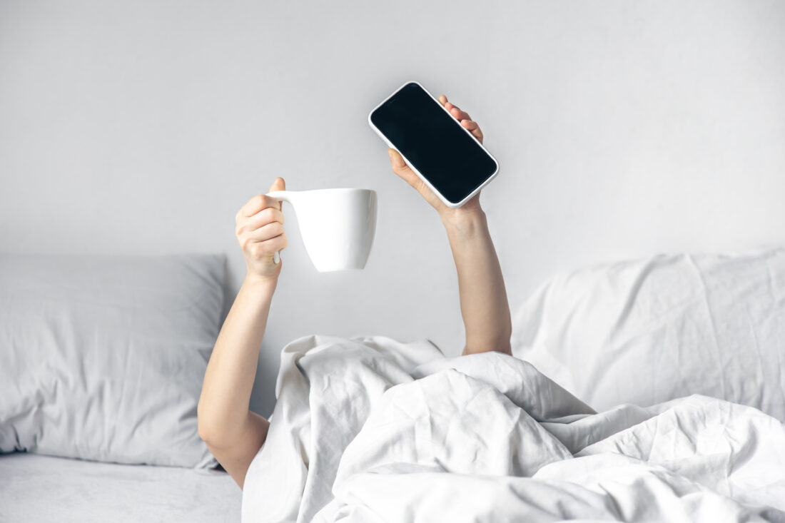 woman lies bed with smartphone cup coffee her hands