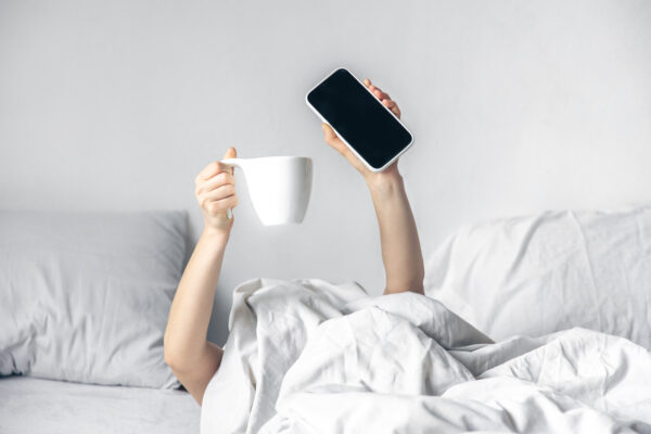 woman lies bed with smartphone cup coffee her hands