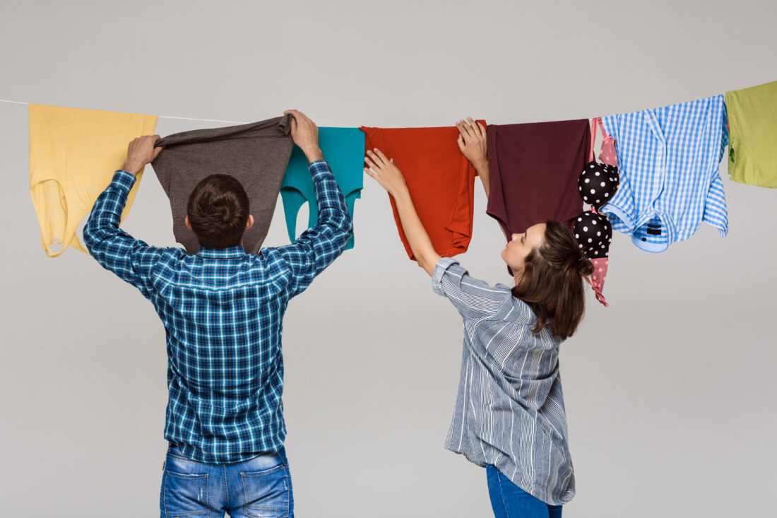 young beautiful couple hanging wash clothes grey wall