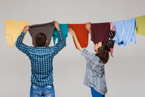 young beautiful couple hanging wash clothes grey wall