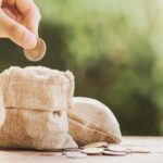 Bukan Menjadi Miskin, Ternyata Berinfaq Bisa Bikin Kaya Raya Lho! 5 067346100 1588740345 Hand Puting Coins In Money Bag For Saving On Table Background