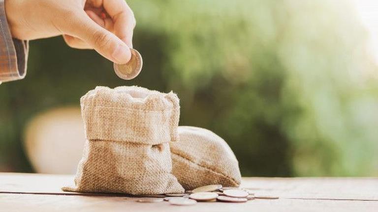 067346100 1588740345 Hand Puting Coins In Money Bag For Saving On Table Background