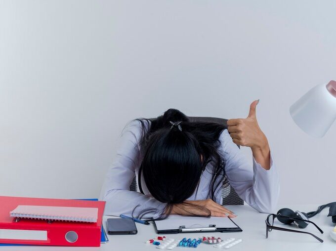 tired young female doctor wearing medical robe stethoscope sitting desk with medical tools putting hand desk head hand showing thumb up isolated 141793 68849