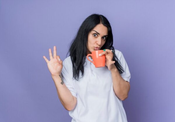 shocked young brunette caucasian girl holds cup gestures ok hand sign isolated purple wall 141793 70398