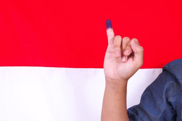man showing finger after voting indonesias presidential election against with indonesia flag 1