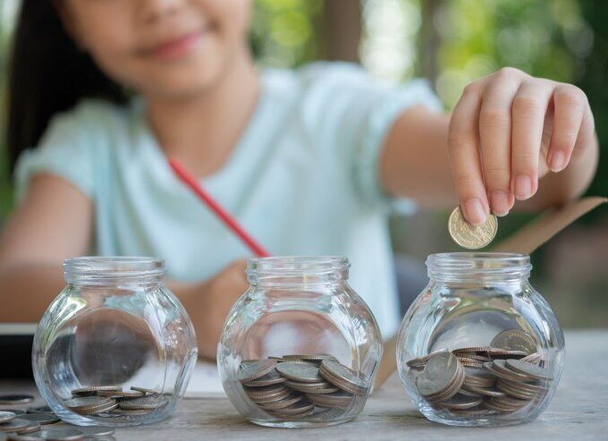 cute asian little girl playing with coins making stacks money kid saving money into piggy bank into glass jar child counting his saved coins children learning about future concept 1150 45703