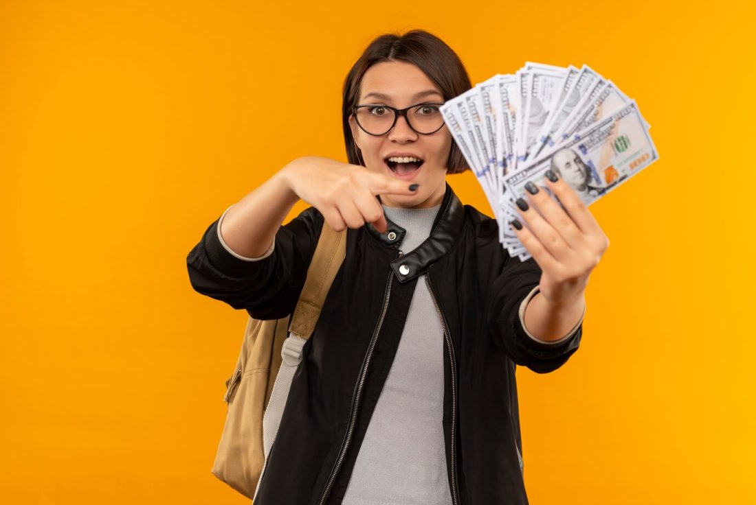 impressed young student girl wearing glasses back bag holding pointing money isolated orange 141793 83841